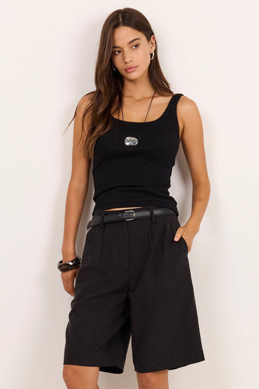 A woman modeling a black sleeveless tank top, black wide-leg shorts, a black belt, and black sandals against a plain off-white studio background.