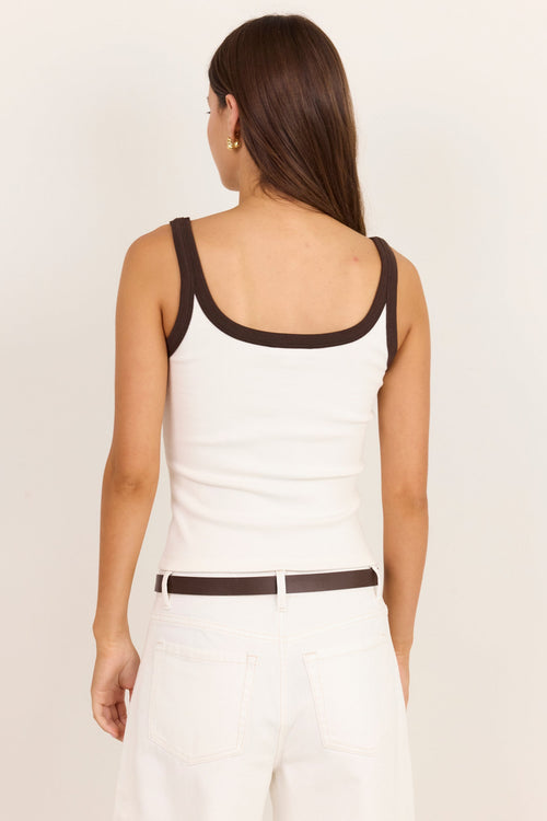 A woman shown from the back wearing a white tank top with dark brown trim and a matching dark brown belt, paired with white pants, against a plain off-white studio background.