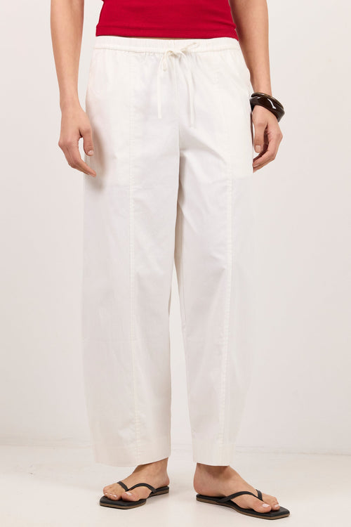A model wearing white wide-leg drawstring pants, a red top, and black flip-flops, standing against a plain white studio background.