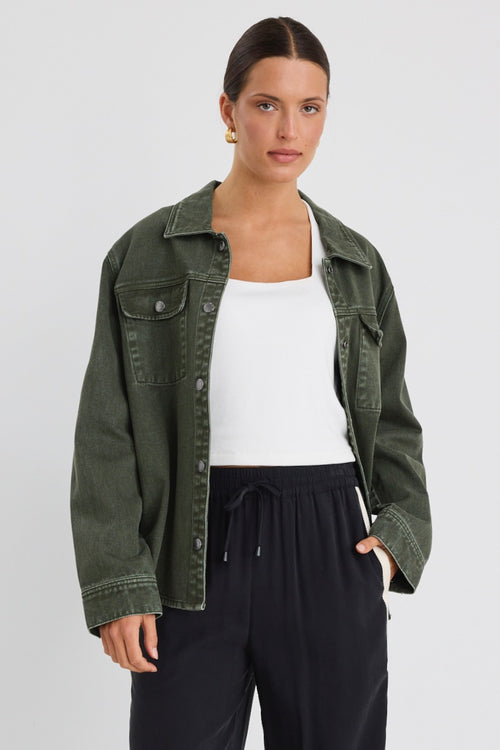 Woman wearing a khaki green washed denim jacket with silver buttons, styled with black pants featuring a cream side stripe.