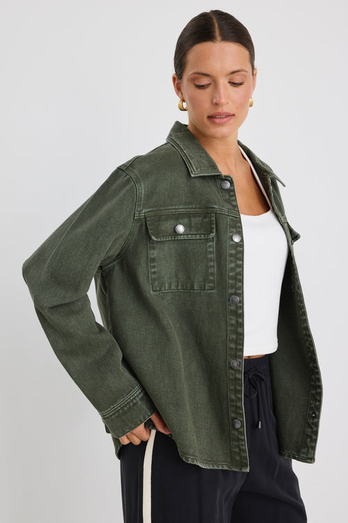 Woman wearing a khaki green washed denim jacket with silver buttons, styled with black pants featuring a cream side stripe.