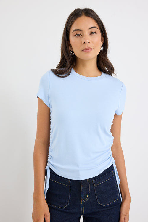 Woman wearing a light blue t-shirt and dark jeans against a plain background