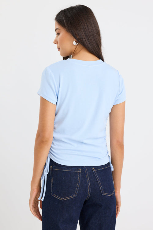 Woman wearing a light blue t-shirt and dark blue jeans on a plain background