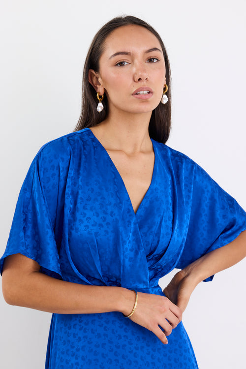 Woman wearing an electric blue satin jacquard midi dress with short kimono sleeves, a wrap-style bodice, and flowing skirt, standing against a white background