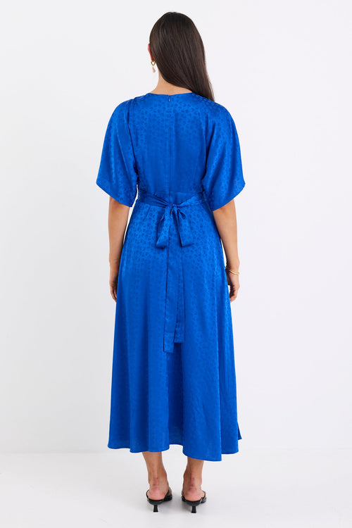 Woman wearing an electric blue satin jacquard midi dress with short kimono sleeves, a wrap-style bodice, and flowing skirt, standing against a white background