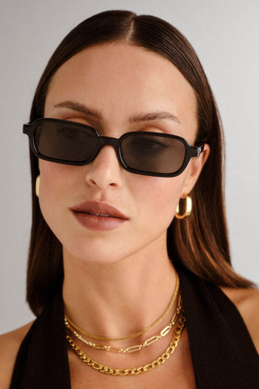 Front-facing view of rectangular sunglasses with a glossy black frame and green-tinted lenses. The slim silhouette features softly rounded corners for a modern take on a retro classic.