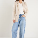 Woman wearing a long-sleeve cream linen blazer with button front and flap pockets, styled with a white top and light blue jeans.