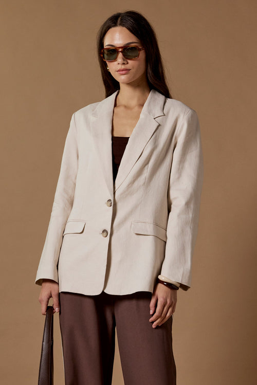 Woman wearing a beige blazer and brown pants against a brown background