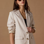 Woman wearing a beige blazer and sunglasses against a brown background