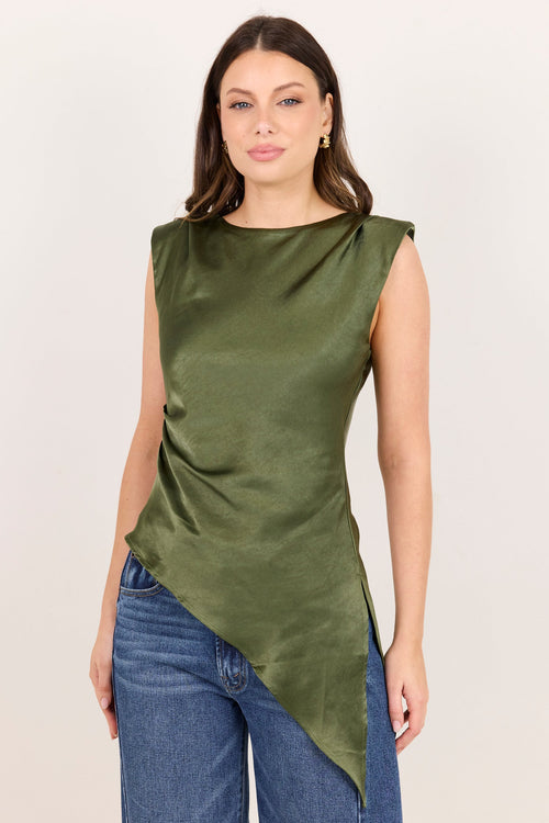 A woman modeling a sleeveless olive green satin top with an asymmetrical draped hem, paired with blue jeans, against a plain off-white background.