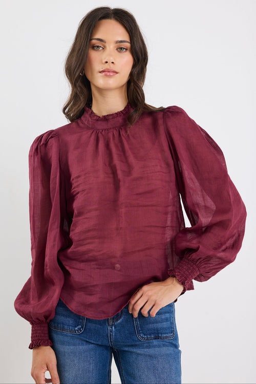 Woman wearing a burgundy blouse with puffed sleeves on a white background