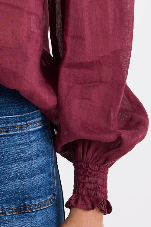 Woman wearing a burgundy blouse with puffed sleeves and blue jeans on a white background