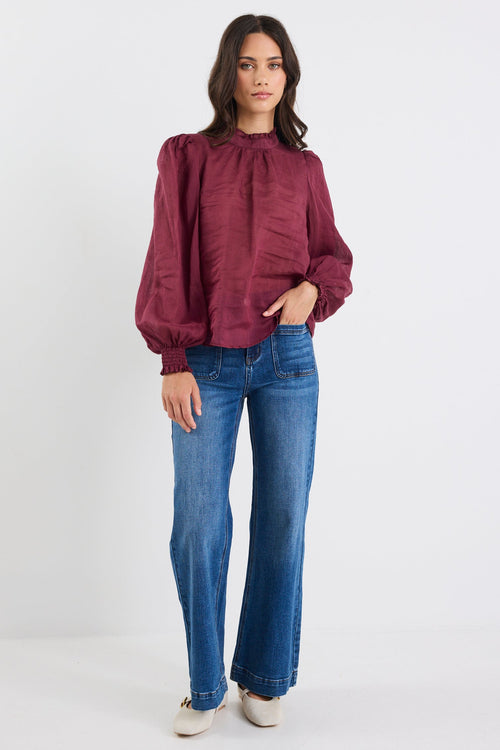 Woman wearing a burgundy blouse and blue jeans on a white background