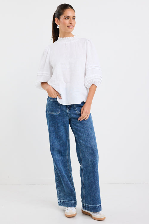 model wears a white linen blouse with dark blue jeans