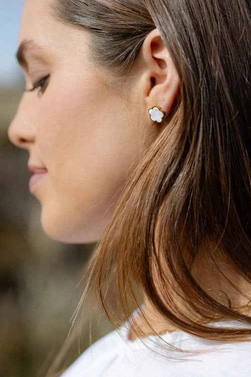 A pair of gold-toned stud earrings shaped like small flowers, featuring a pearlescent centre framed by a polished gold outline for a soft, elegant finish