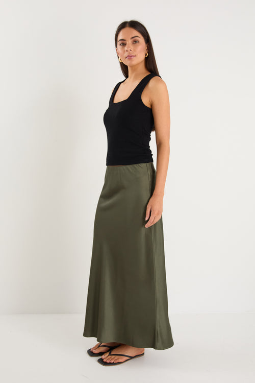 the model wears a khaki green maxi skirt with a black tank top
