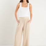 Woman wearing a white tank top and beige wide-leg pants on a white background