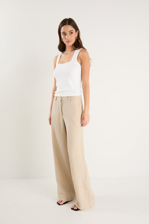 Woman wearing a white tank top and beige pants on a white background