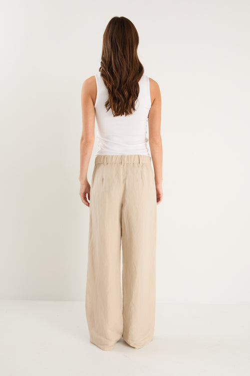 Woman wearing a white sleeveless top and beige wide-leg pants on a white background