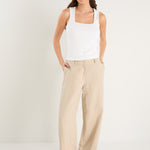 Woman wearing a white tank top and beige pants on a white background