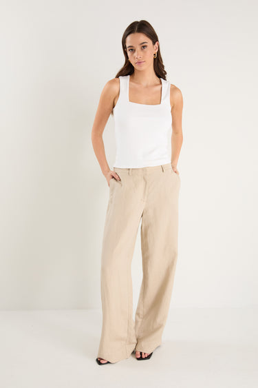 Woman wearing a white tank top and beige pants on a white background