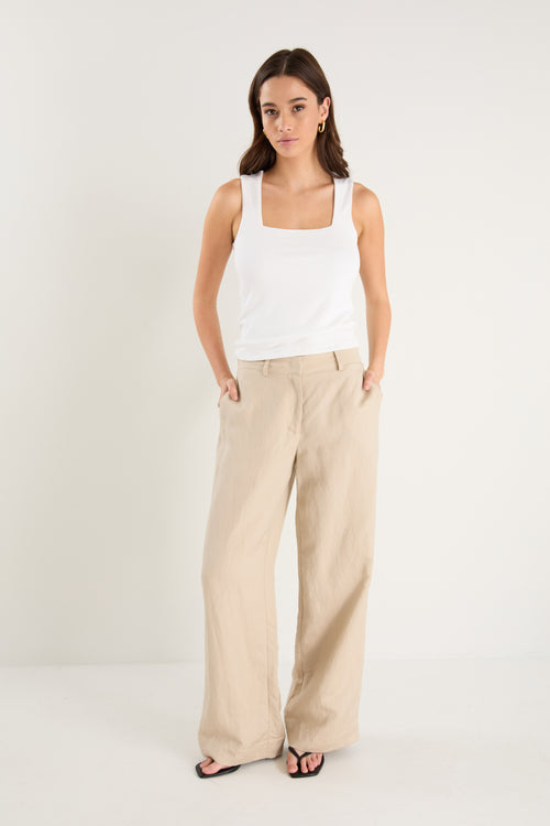 Woman wearing a white sleeveless top and beige pants on a white background