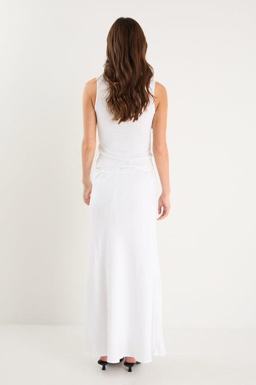 The model wears a white linen maxi skirt with a white tank top