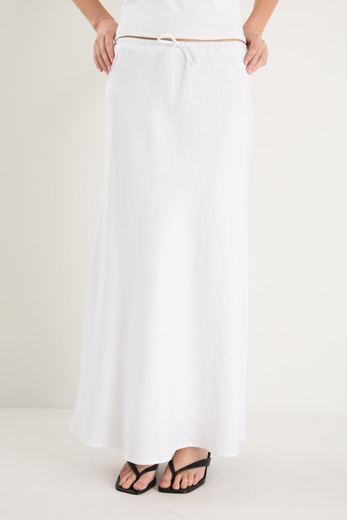The model wears a white linen maxi skirt with a white tank top