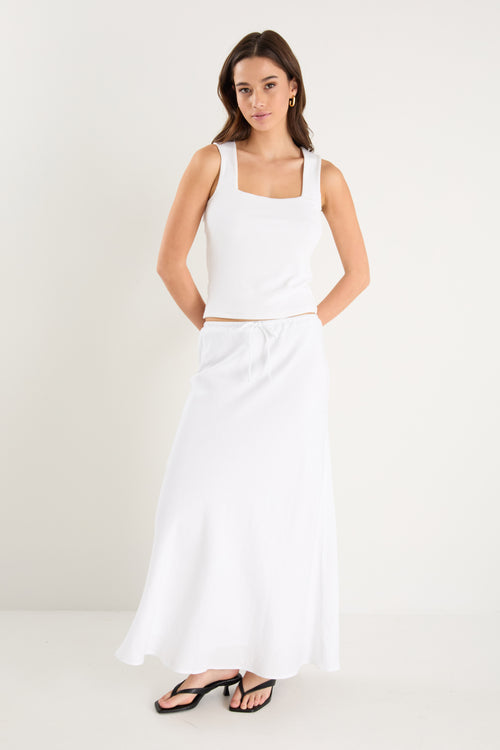 The model wears a white linen maxi skirt with a white tank top