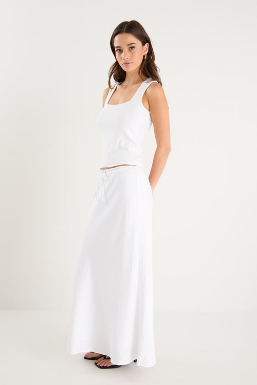 The model wears a white linen maxi skirt with a white tank top