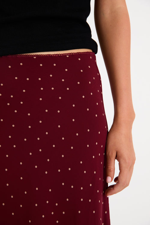 Model wearing a burgundy polka dot satin midi skirt with a bias-cut silhouette and a soft drape