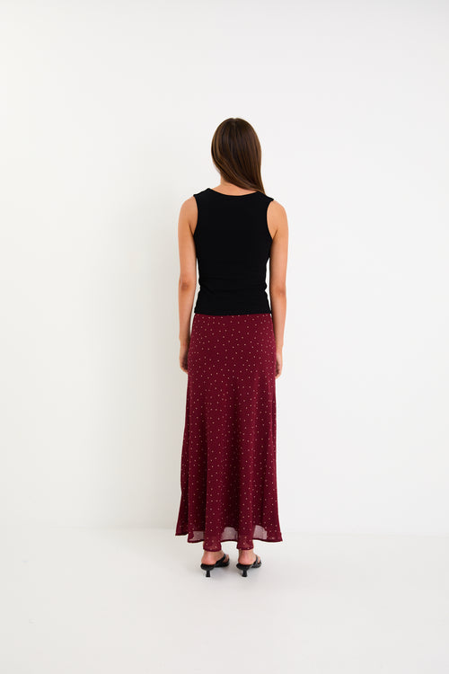 Model wearing a burgundy polka dot satin midi skirt with a bias-cut silhouette and a soft drape