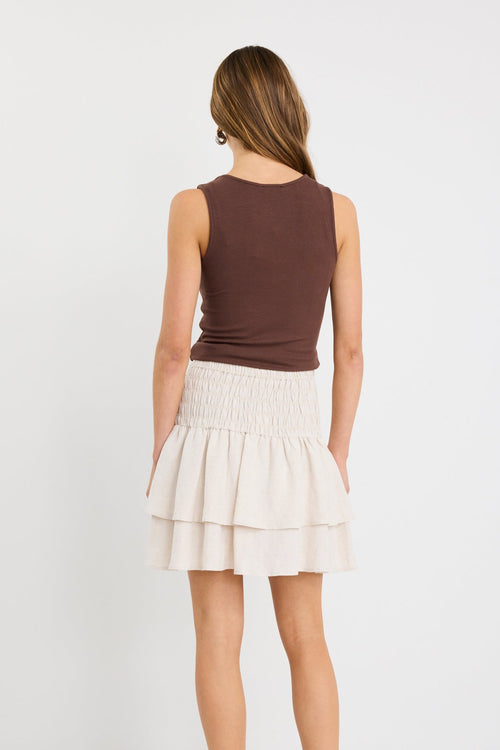 Woman wearing a natural tiered linen-blend mini skirt with a shirred waistband and layered hem, styled with a chocolate tank.