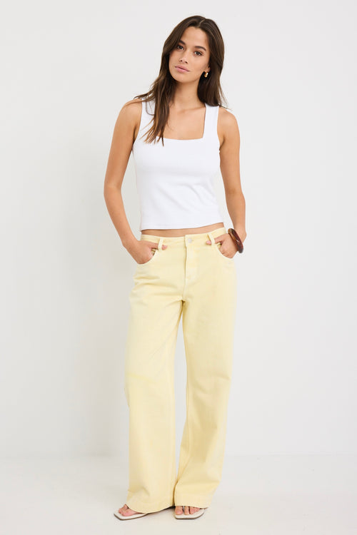 Woman wearing mid-rise wide-leg jeans in a plain butter-yellow wash, styled with a simple white tank and sandals.