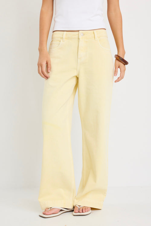Woman wearing mid-rise wide-leg jeans in a plain butter-yellow wash, styled with a simple white tank and sandals.