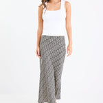 Woman wears a black white geometric print skirt and white tank with black thong heels