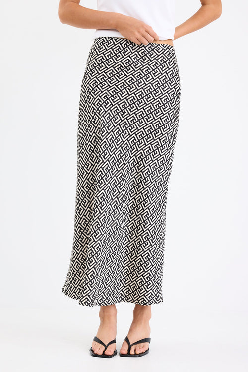 Woman wears a black white geometric print skirt and white tank with black thong heels