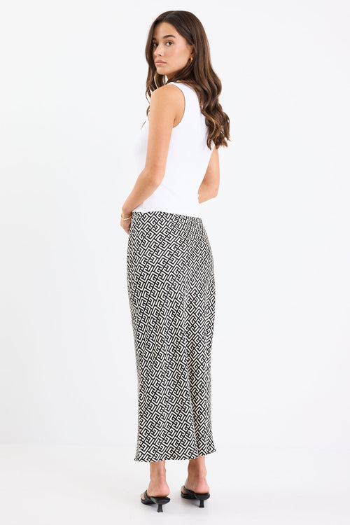 Woman wears a black white geometric print skirt and white tank with black thong heels