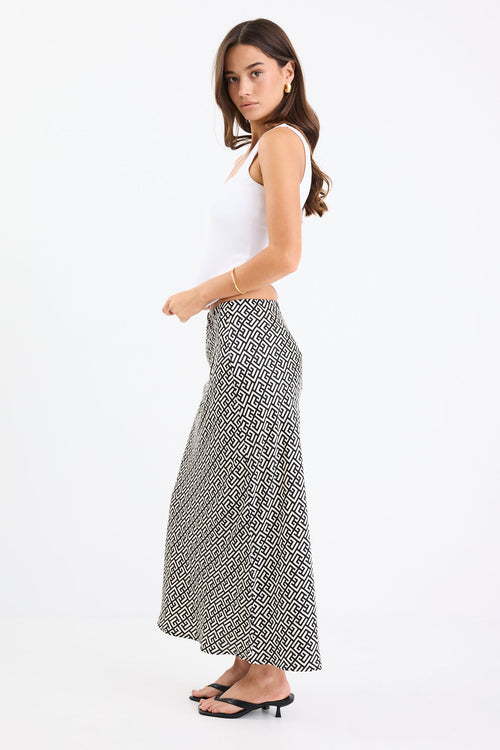 Woman wears a black white geometric print skirt and white tank with black thong heels