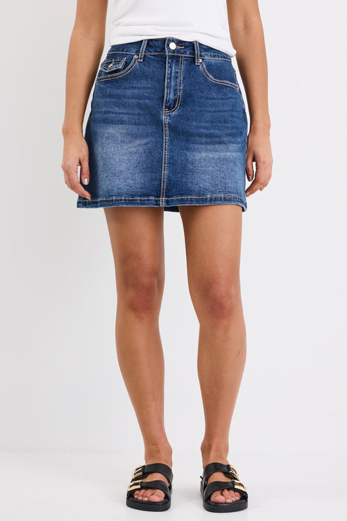 A mid-blue mini skirt with front pockets, made from a stretchy cotton blend. Features a classic denim wash, with 99% cotton and 1% elastane for a comfortable, breathable fit.