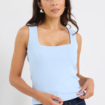 woman wearing a pale blue square-neck sleeveless tank paired with indigo jeans