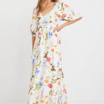 Woman wearing a cream midi dress with a sweetheart neckline, puff sleeves, elastic waist, and garden floral print in red, yellow, and blue tones.
