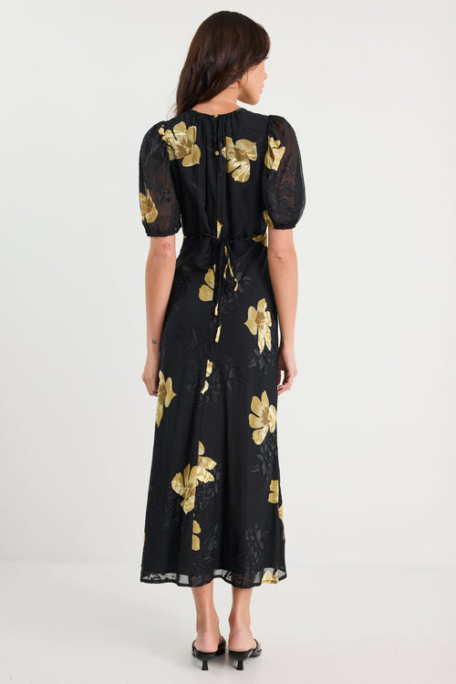 Woman wearing a black dress with gold floral patterns on a white background
