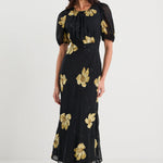 Woman wearing a black dress with gold floral patterns on a white background