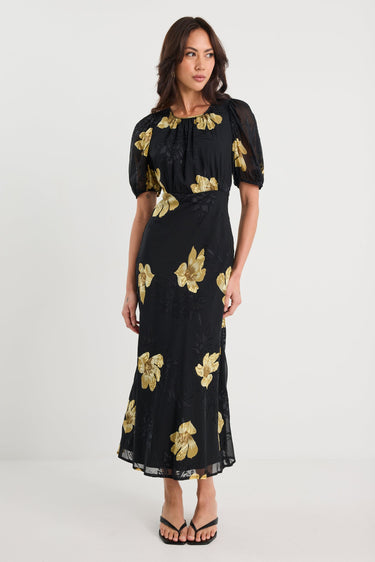 Woman wearing a black dress with gold floral patterns on a white background