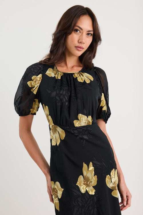 Woman wearing a black dress with gold floral patterns on a white background