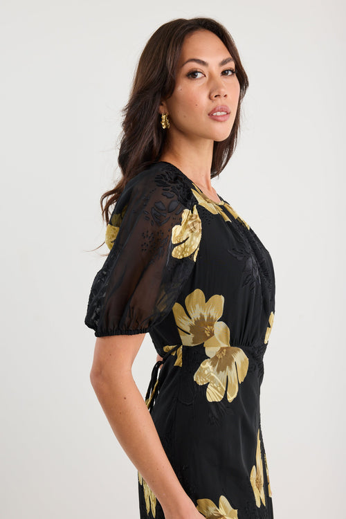 Woman wearing a black dress with gold floral patterns on a white background