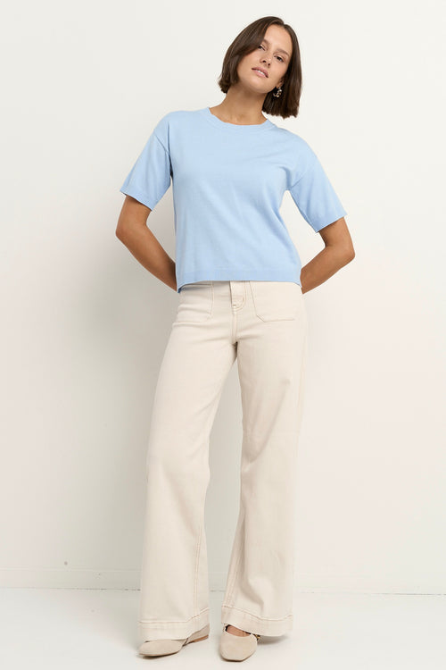model wears a light blue knit t-shirt with ecru wide leg jeans