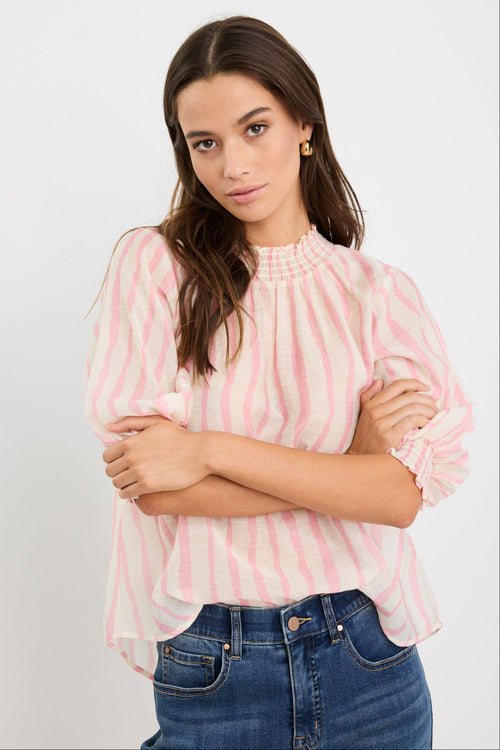Woman wearing a blush and ivory stripe short sleeve top with a high neck and relaxed fit, styled with blue jeans.