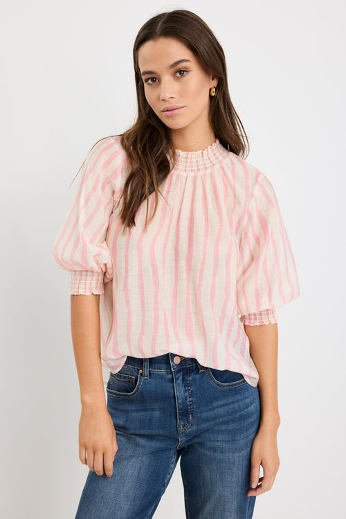 Woman wearing a blush and ivory stripe short sleeve top with a high neck and relaxed fit, styled with blue jeans.